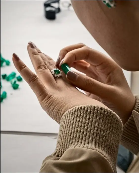 Hands holding a cut emerald over a tray of stones