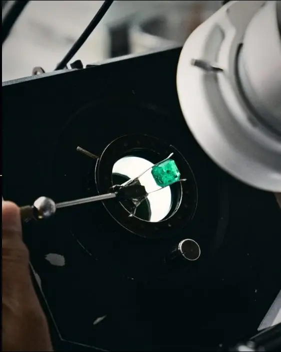 An emerald held in a dop under the cutting microscope light